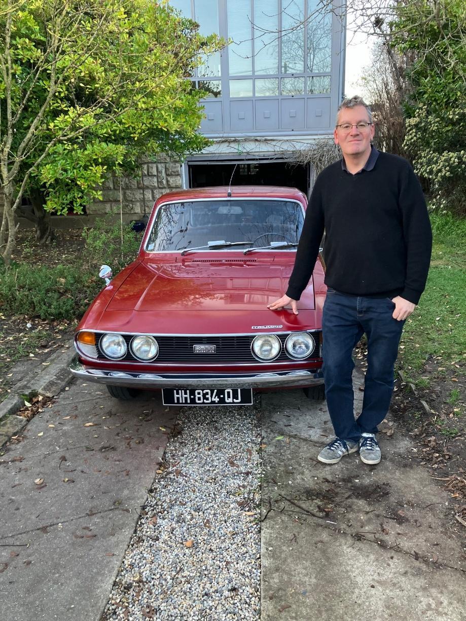 Simon Williams standing proudly beside his restored red Triumph 2500PI